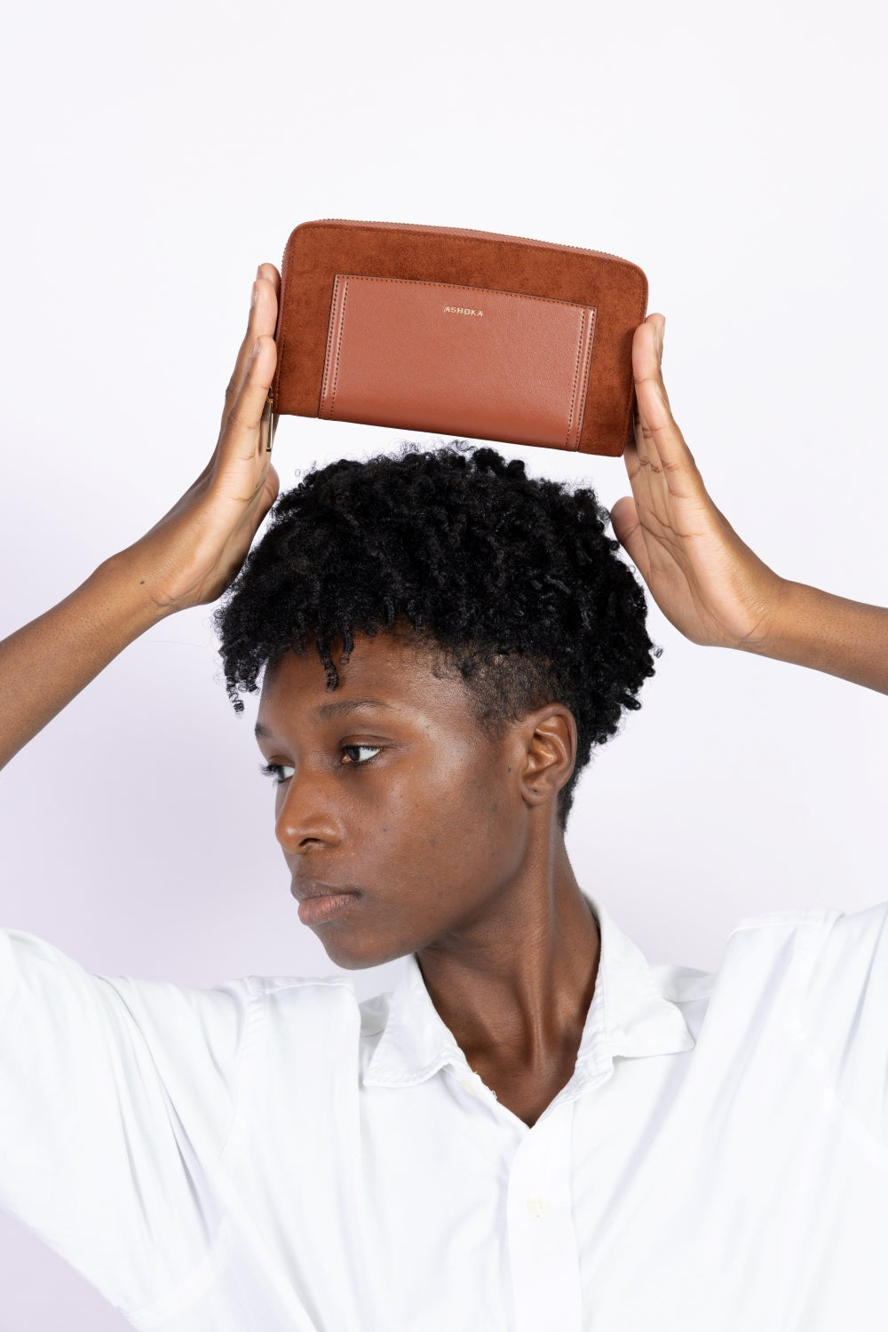 Portefeuille Compagnon vegan Ashoka Paris en cuir végétal camel avec fermeture zippée, tenu à la main au-dessus de la tête, représentant la collection portefeuilles.