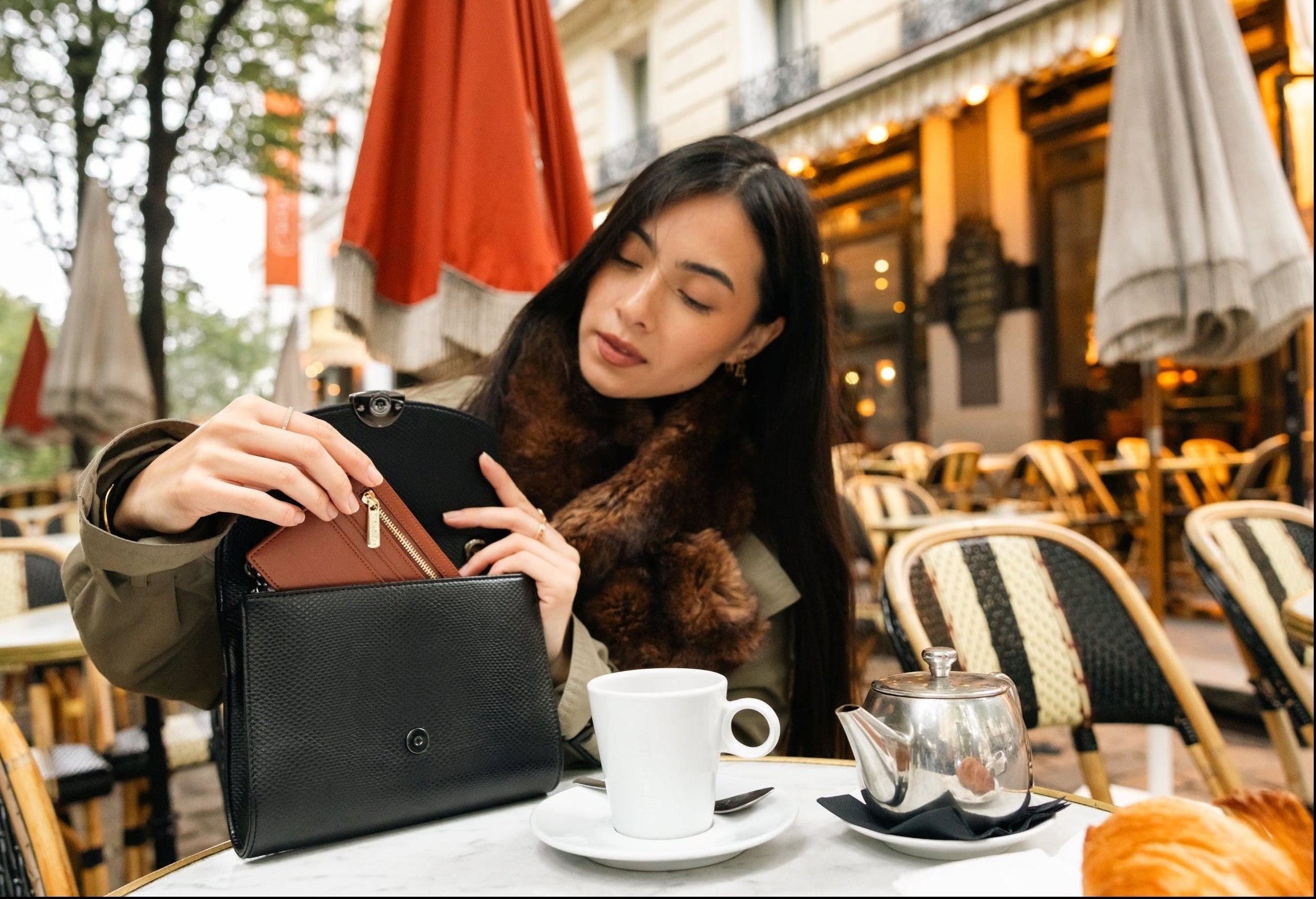 Porte-carte zippé camel introduit dans un Mini Paname Lézard Noir par une femme dans un café parisien pour la homepage Ashoka Paris